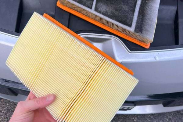 Un filtre à air neuf et un filtre usé posés sur une voiture.