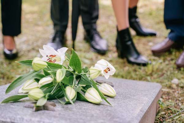 Des fleurs blanches sont posées sur une tombe entourée de proches en deuil.