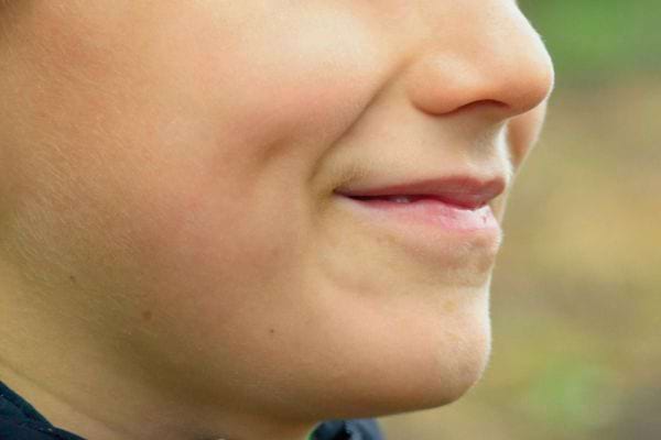Un enfant sourit discrètement, laissant apparaître de petites fossettes.