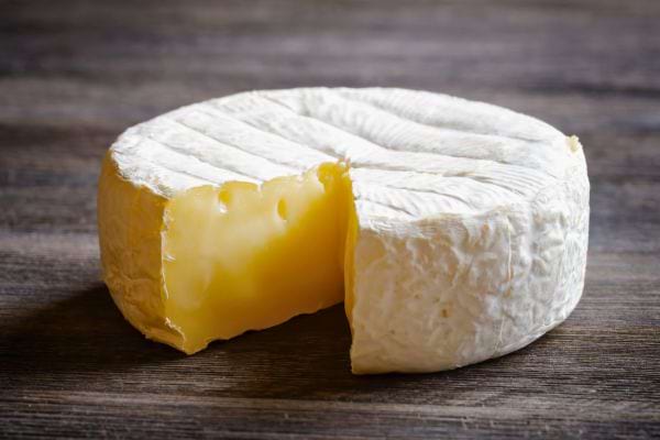 Un camembert entier avec une part coupée révèle sa pâte jaune crémeuse.