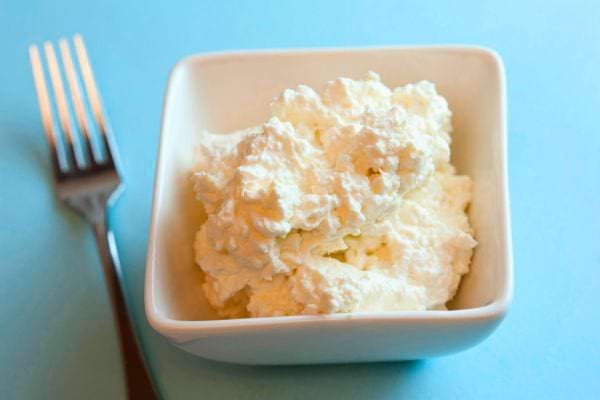 Un bol blanc contient du fromage cottage à la texture granuleuse, accompagné d’une fourchette.