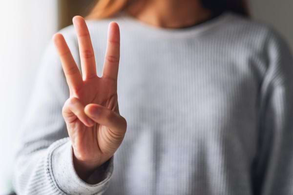Une personne montre trois doigts avec sa main.