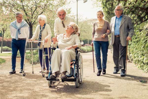 Groupe de personnes âgées marchant, dont une femme en fauteuil roulant.