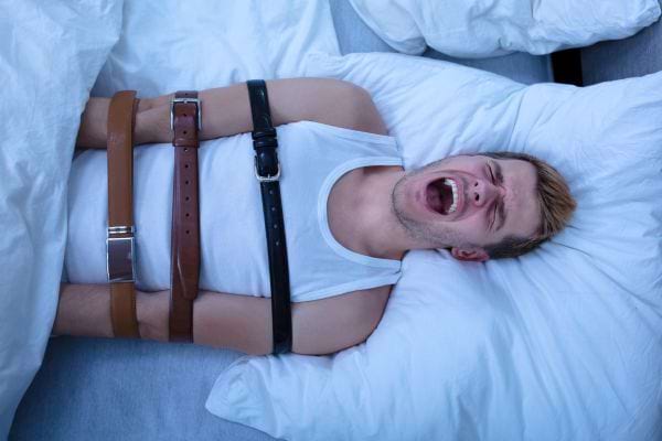Un homme attaché au lit par des ceintures, criant de peur.
