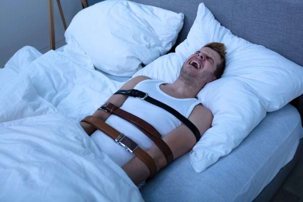 Un homme allongé, attaché avec des ceintures, hurlant de terreur.