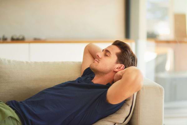 Un homme détendu repose confortablement sur un canapé, les bras derrière la tête et les yeux fermés.