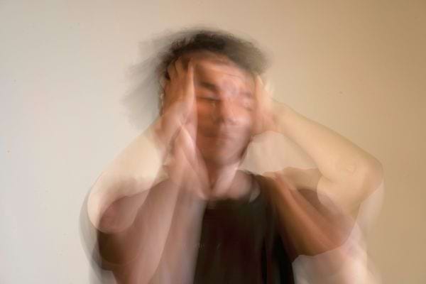 Un homme flou se tient la tête avec les deux mains, évoquant un vertige ou une migraine.