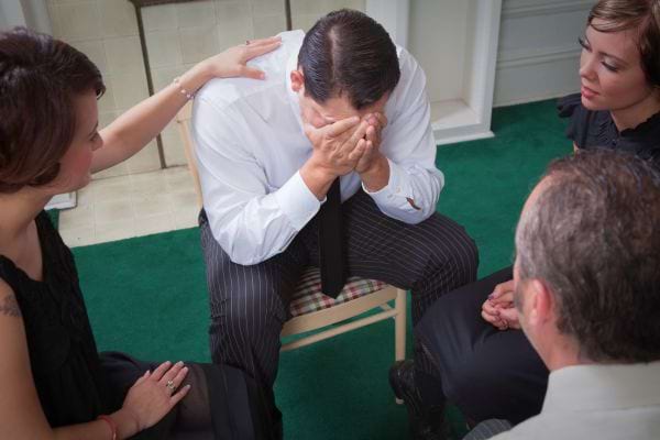Un homme en costume pleure entouré de proches.