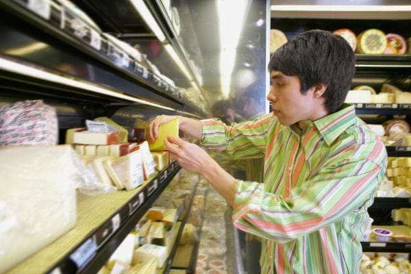 Un homme choisit un fromage emballé dans le rayon frais d’un supermarché.