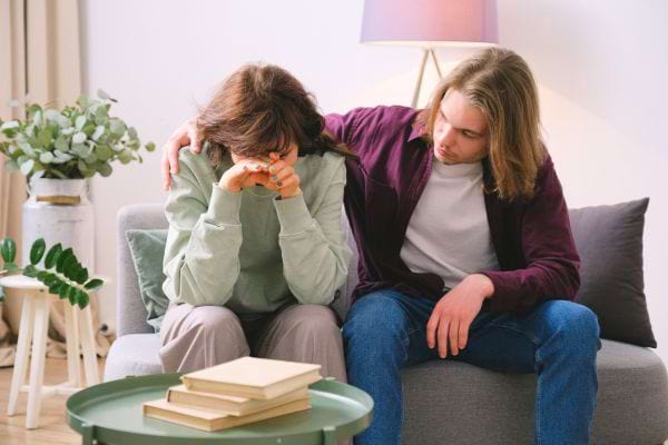 Un jeune homme réconforte une femme en larmes sur un canapé.