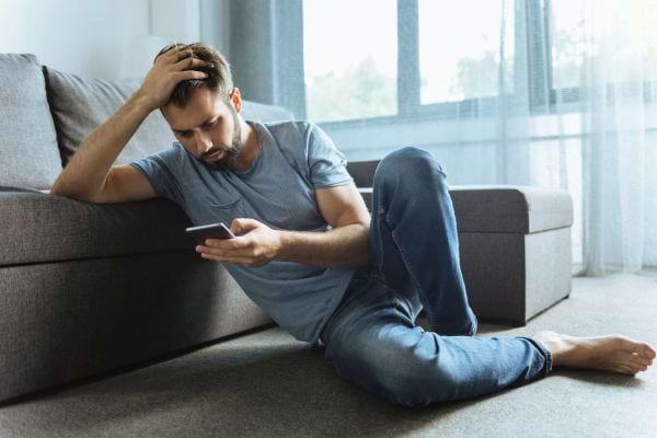 Un homme assis au sol regarde son téléphone, bouleversé.
