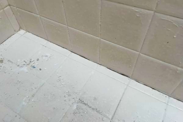 Des joints de carrelage jaunis et encrassés apparaissent au sol d’une douche mal entretenue.