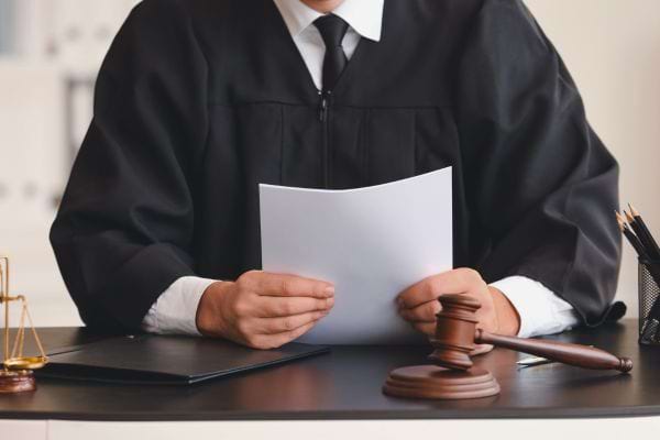 Un juge en robe noire lit un document derrière son bureau avec un marteau de justice.
