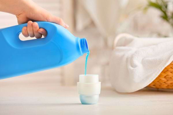 Une main verse de la lessive liquide bleue dans un bouchon doseur.