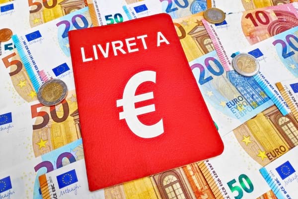 Un livret A rouge posé sur plusieurs billets en euros.