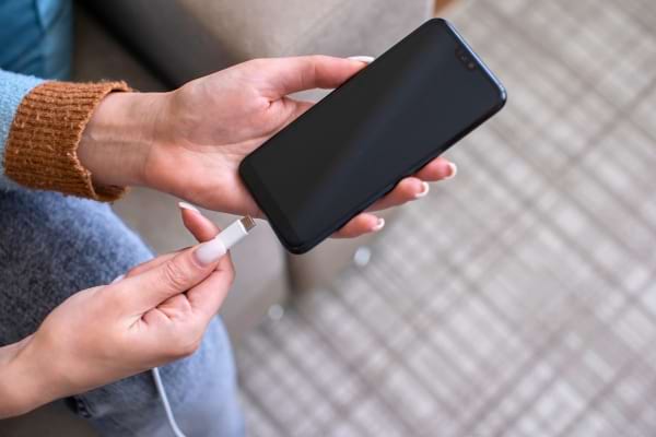 Main tenant un câble USB prêt à être branché dans un smartphone.