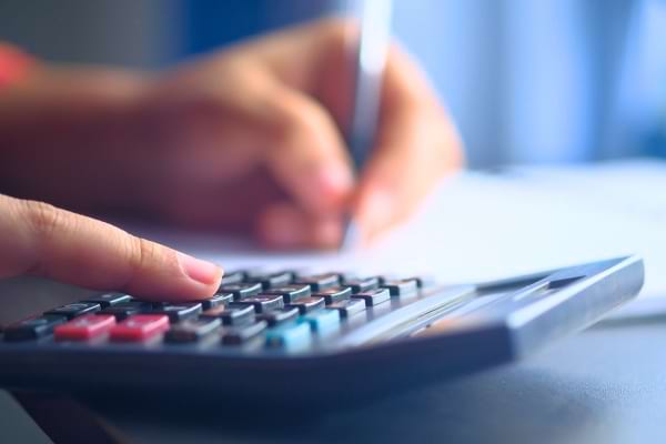 Main appuyant sur une calculatrice avec stylo en arrière-plan.