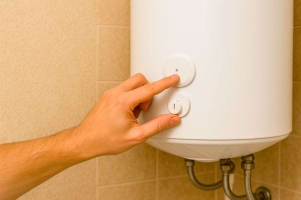 Un doigt appuie sur le bouton d’arrêt d’un chauffe-eau pour l’éteindre et éviter de gaspiller de l’énergie inutilement.