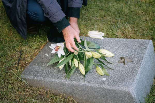 Une main dépose des lys blancs sur une tombe.
