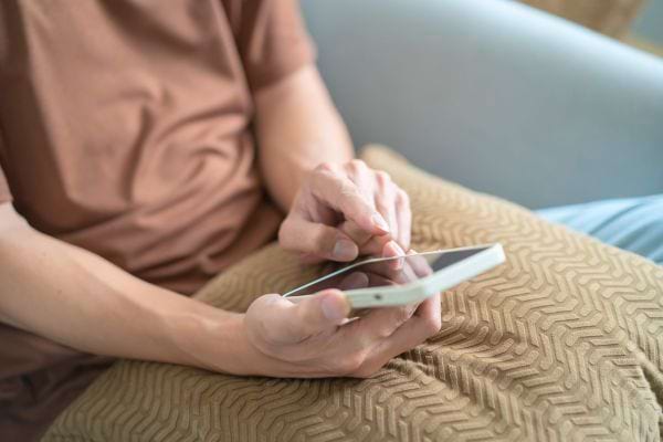 Un homme en t-shirt manipule son smartphone posé sur un coussin.