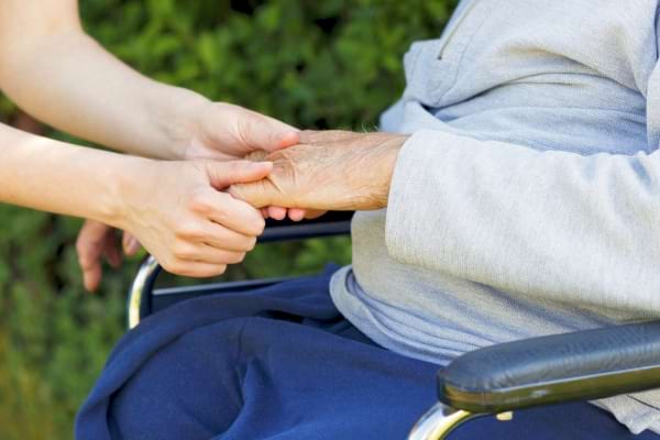 Une personne tient la main d’un senior assis en fauteuil roulant.