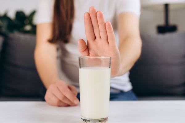 Une personne fait un geste de refus devant un verre de lait posé sur la table.