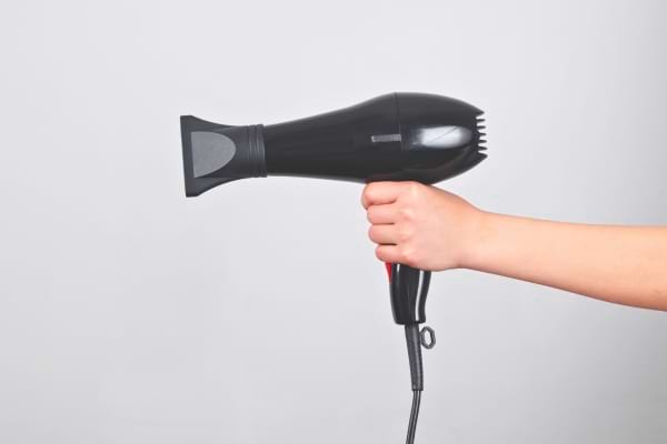 Une main tient un sèche-cheveux noir prêt à être utilisé.