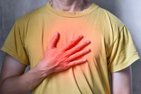 Une main posée sur une poitrine illuminée en rouge, représentant une douleur cardiaque ou une alerte de santé.