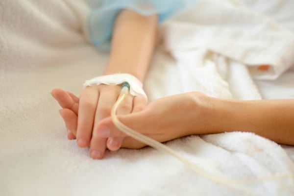 Deux mains se tiennent, l’une perfusée, sur un lit d’hôpital.