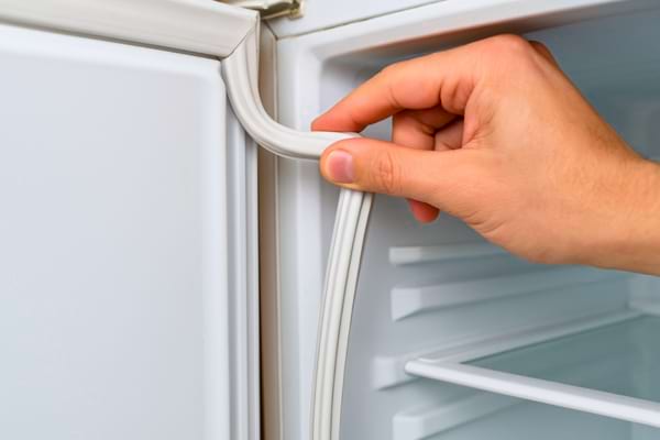 Un homme soulève le joint en caoutchouc d’une porte de congélateur pour le vérifier.