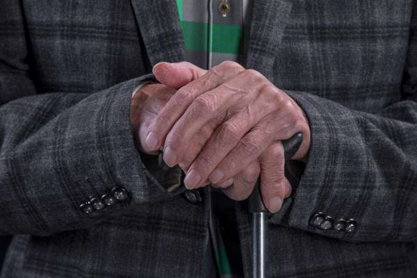 Mains ridées posées sur une canne, symbole de vieillesse et de soutien.