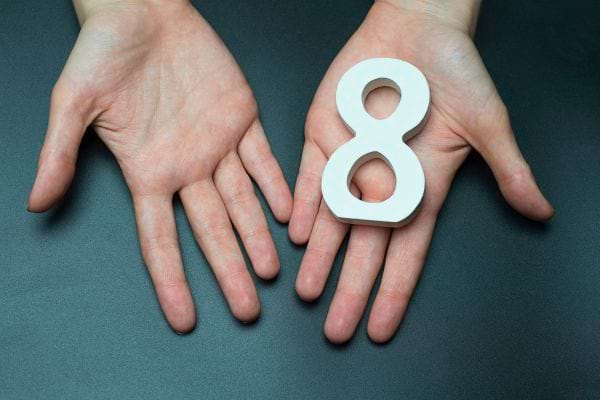 Deux mains tiennent le chiffre huit blanc en plastique.