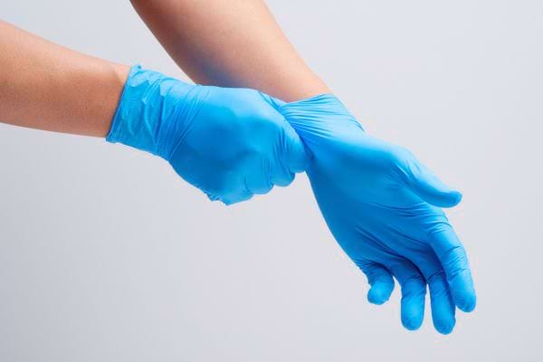 Une personne enfile des gants de protection bleus.