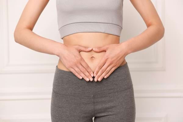 Une femme forme un cœur avec ses mains posées sur son ventre.