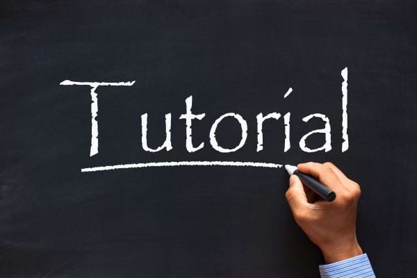 Une main écrit le mot « Tutorial » à la craie blanche sur un tableau noir.