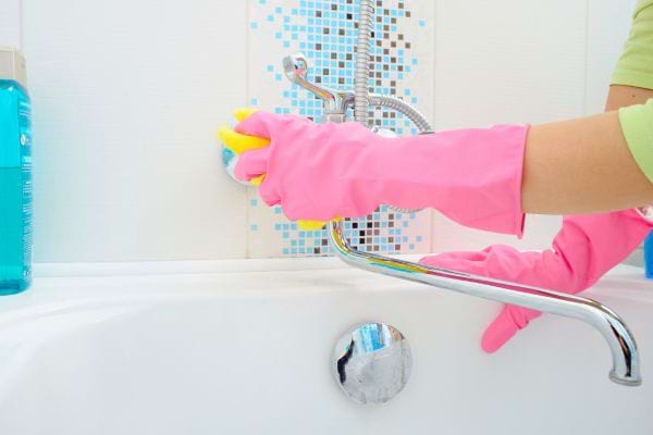 Une personne nettoie une baignoire avec des gants roses.