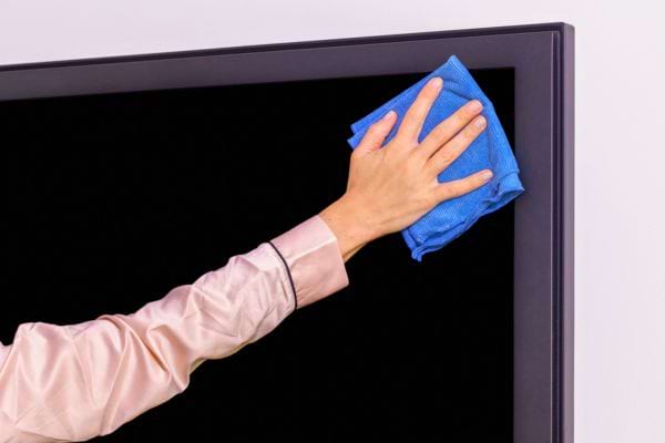 Une main essuie l’écran d’une télévision avec un chiffon bleu.