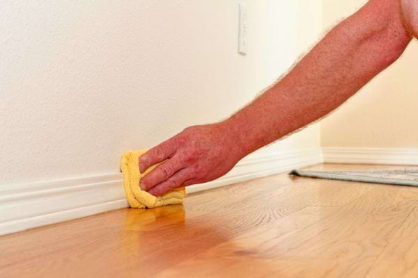 Main essuyant une plinthe avec un chiffon jaune.