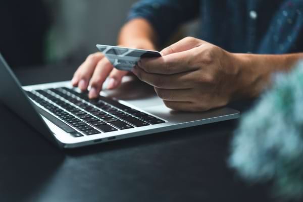 Une personne saisit une carte bancaire devant son ordinateur portable.