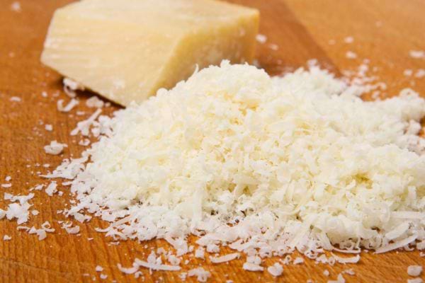 Du parmesan râpé en copeaux fins repose sur une planche en bois avec un morceau de fromage.