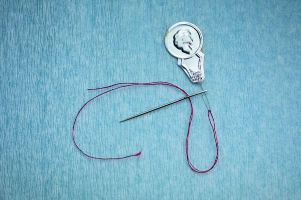 Un passe-fil métallique inséré dans une aiguille avec du fil rose.