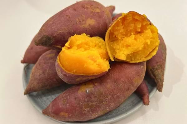 Une assiette de patates douces violettes, l’une ouverte révélant une chair orange cuite.