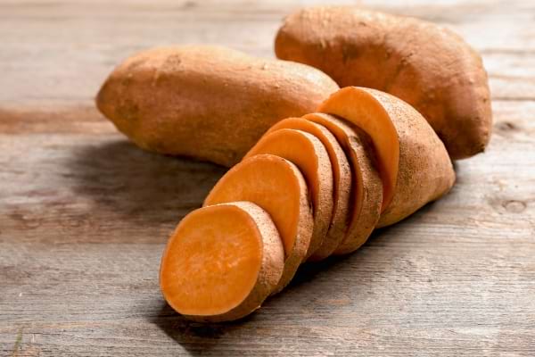 Des patates douces brunes, l’une tranchée en rondelles sur une planche.