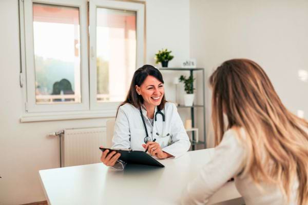 Une patiente sourit en discutant avec une femme médecin assise derrière son bureau.