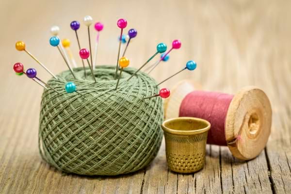 Une pelote verte avec épingles colorées, un dé à coudre et une bobine de fil.
