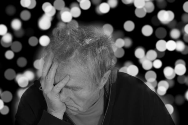 Un senior se tient le visage d’une main, l’air fatigué et triste.