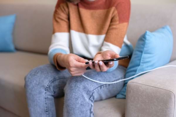 Personne assise branchant son téléphone avec un câble de recharge.