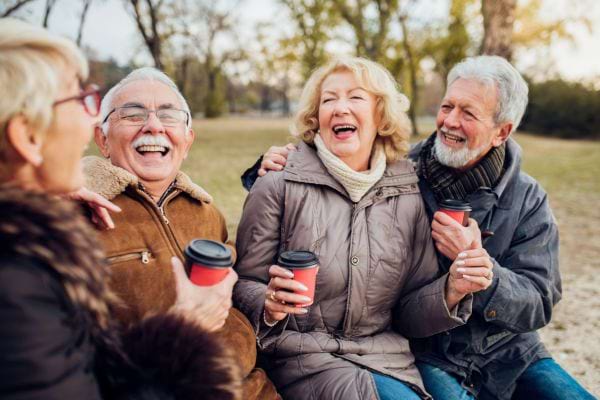 Quatre seniors rient ensemble en buvant du café dehors.