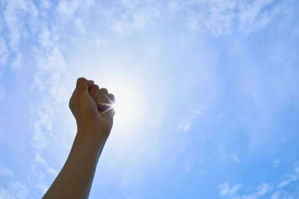 Un poing levé vers le ciel ensoleillé, symbole de force et de détermination.