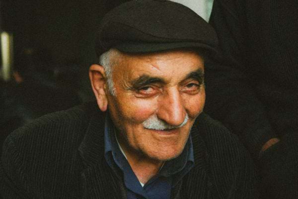 Portrait d’un homme âgé souriant, portant une casquette sombre.